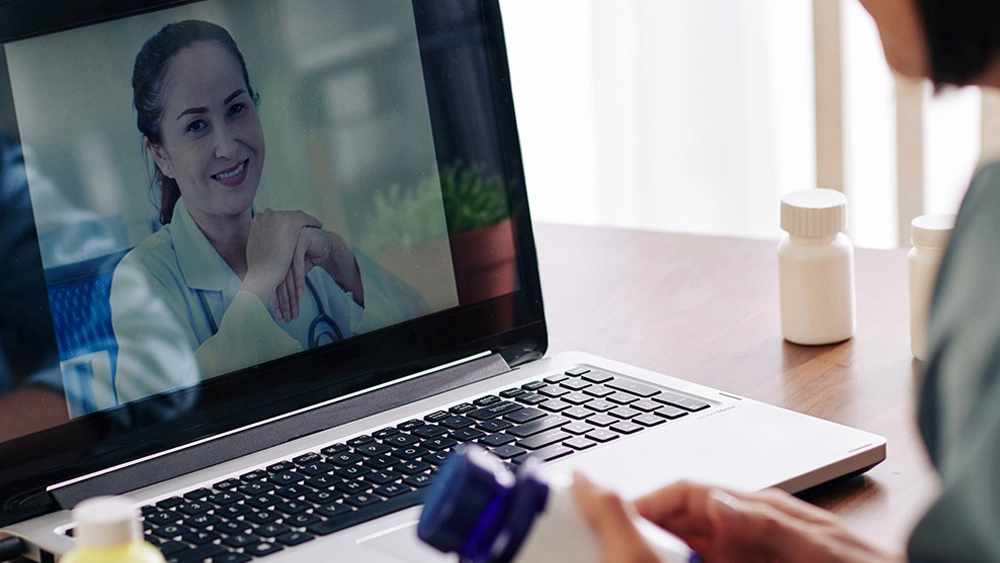 Picture of woman on a laptop with a doctor on the screen for a Telehealth appointment.