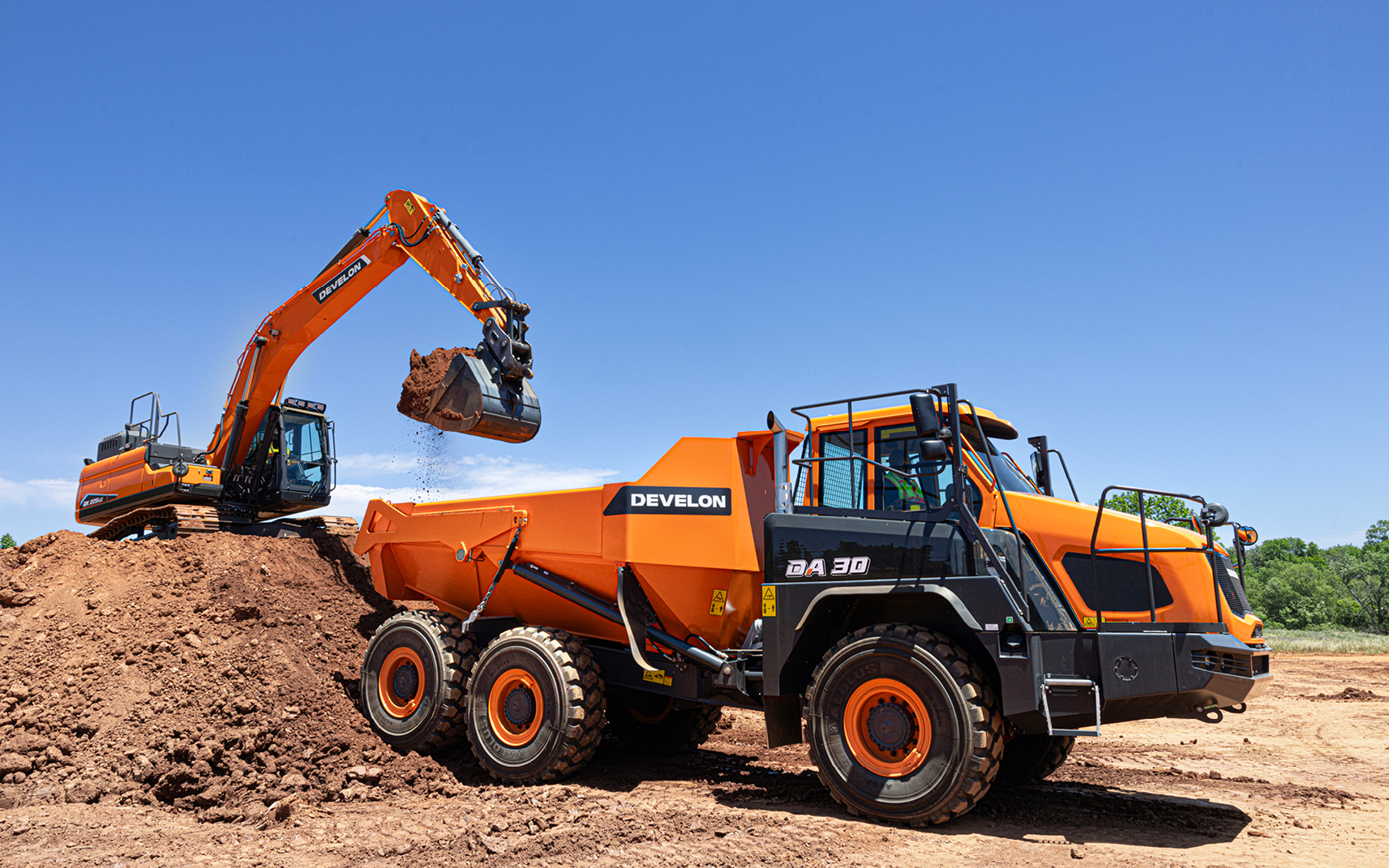 An excavator loads an ADT. Proper usage of machines can lead to a higher construction equipment resale value.