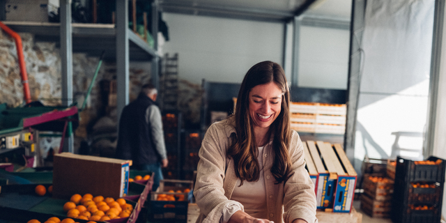 Woman filling boxes of oranges in warehouse