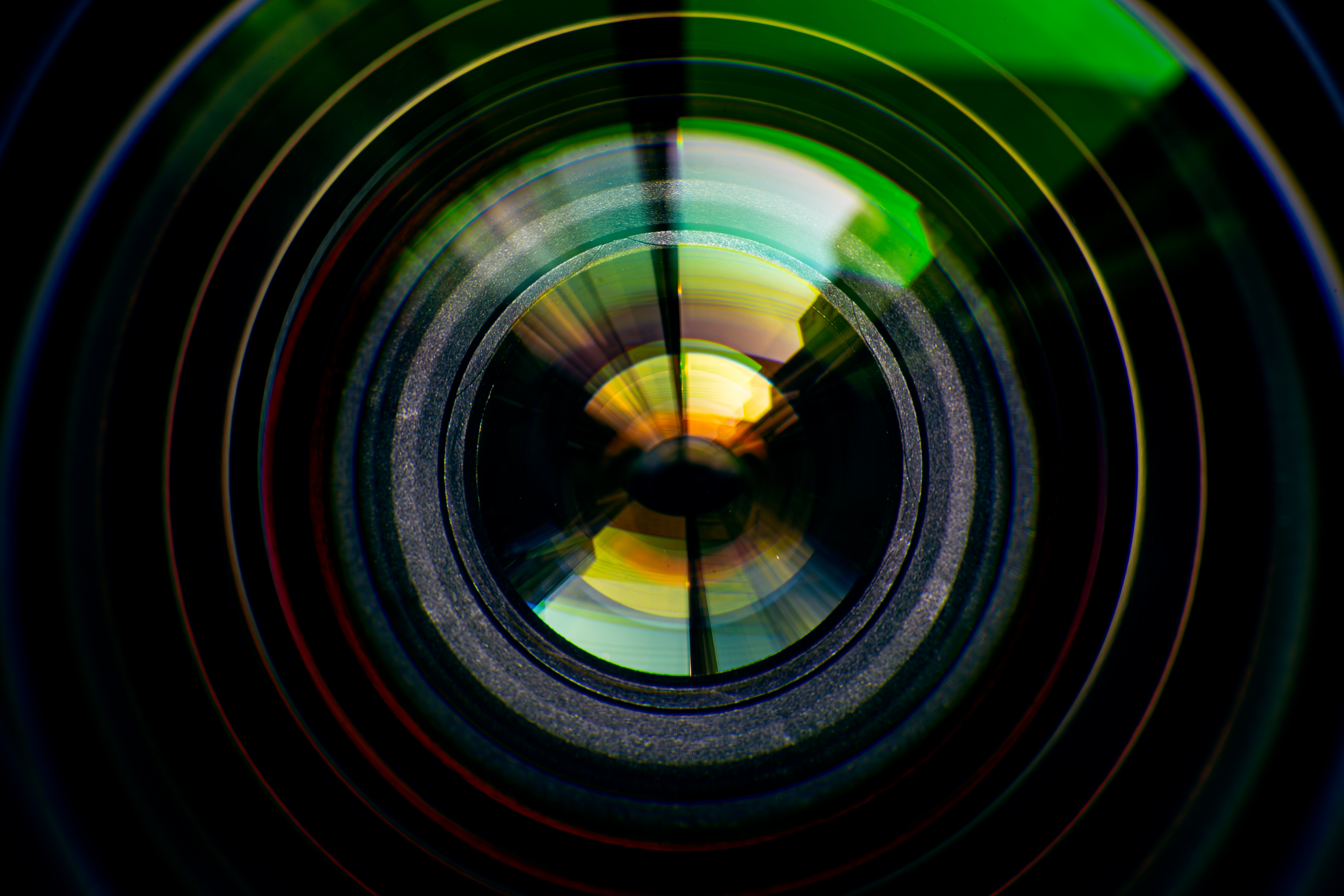 The lens of a 4k studio camera with auto focus in close detail, with rainbow light effects reflecting off of it.