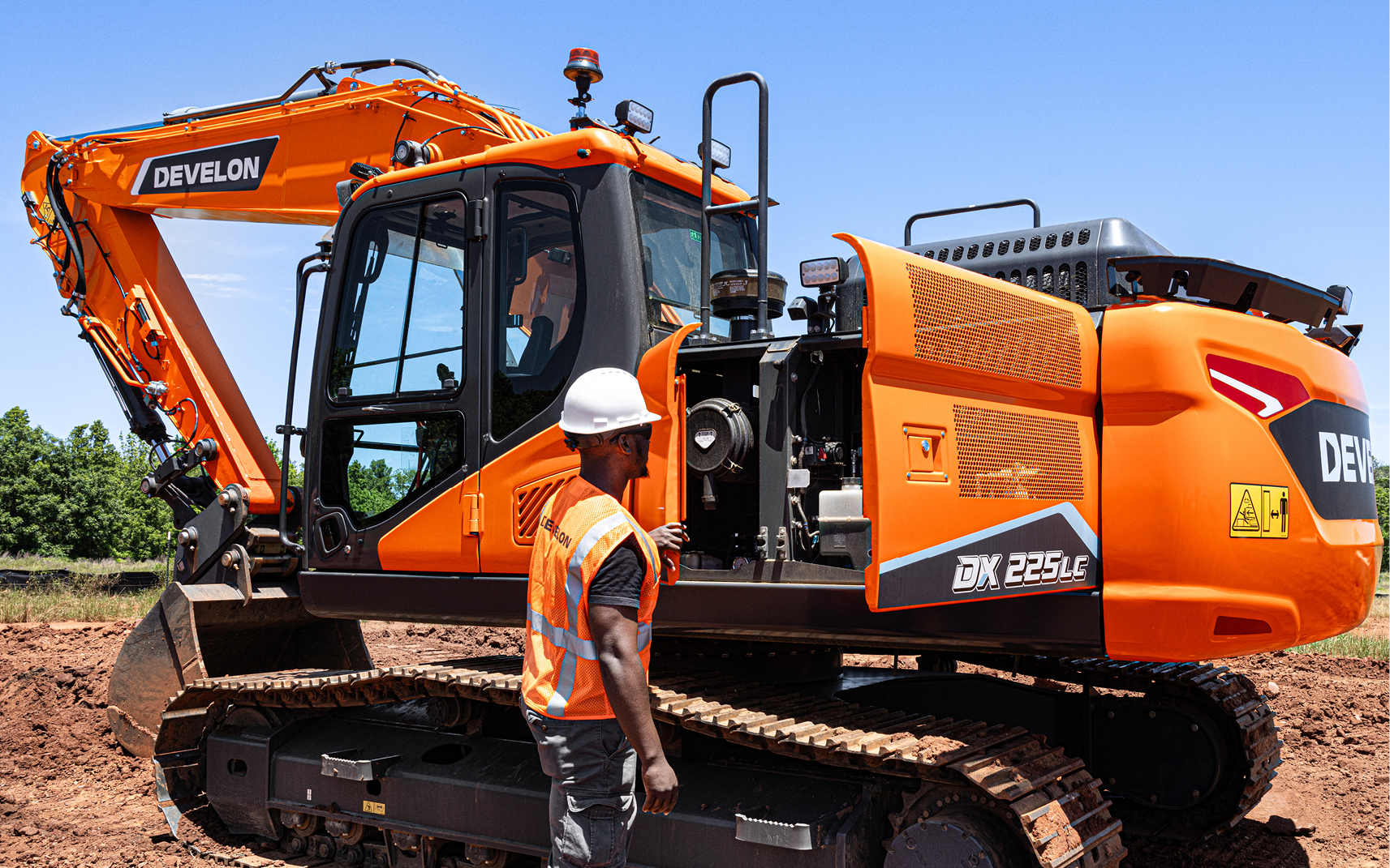An operator inspecting the internal components of a DEVELON DX225LC-7 crawler excavator.