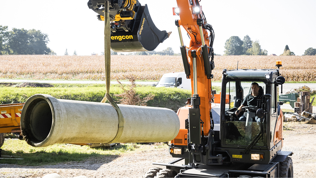 A DEVELON wheel excavator moving a large pipe on a job site.