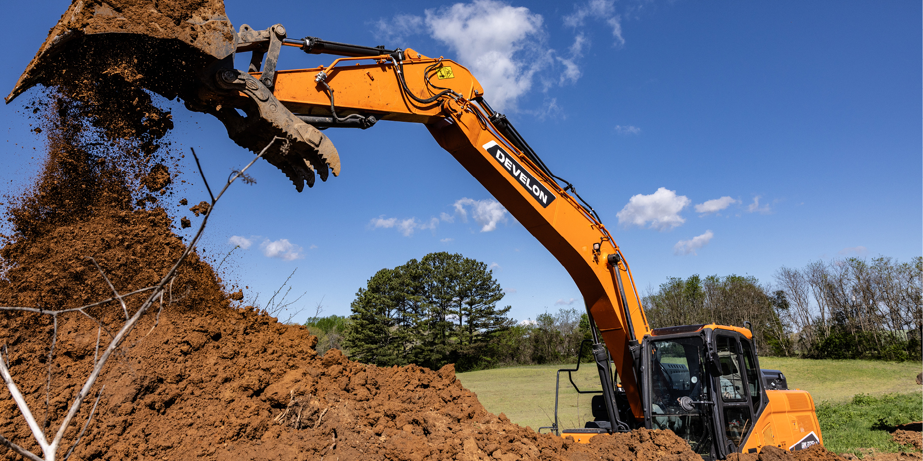 A DEVELON crawler excavator dumping dirt on a job site.