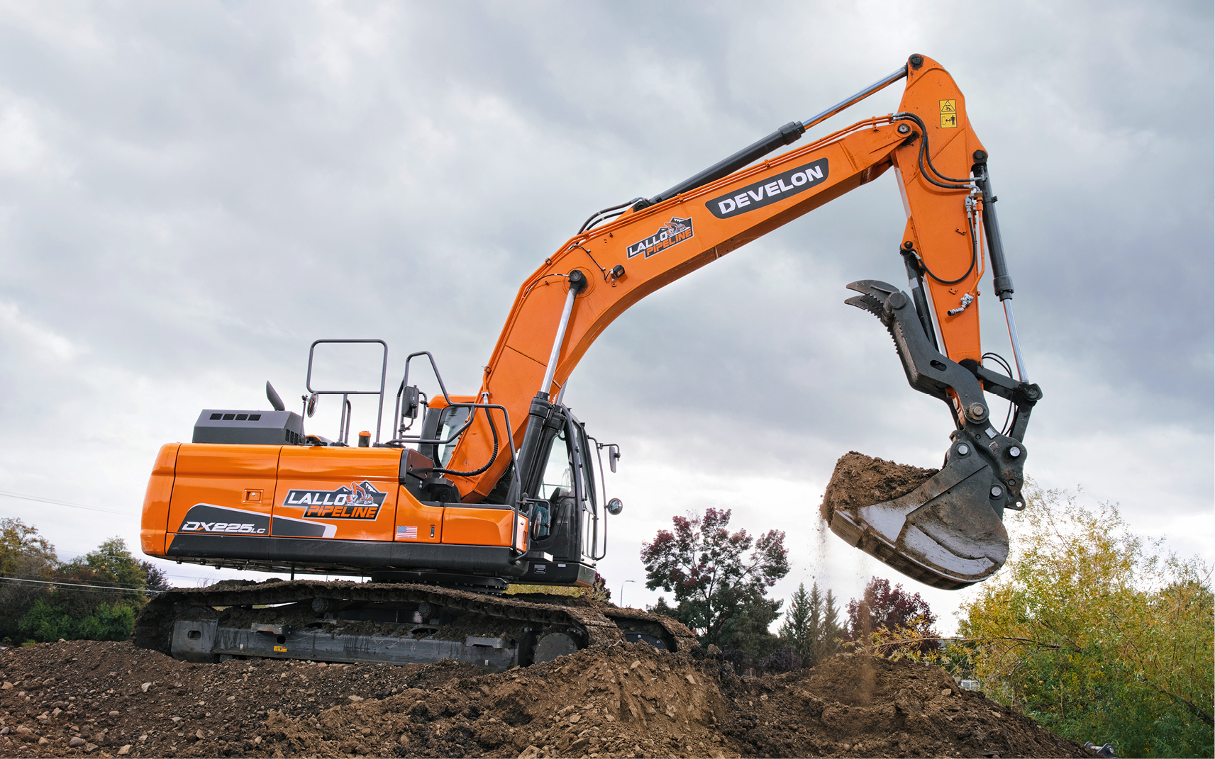 A DEVELON DX225LC-7 crawler excavator lifts a bucket of dirt.