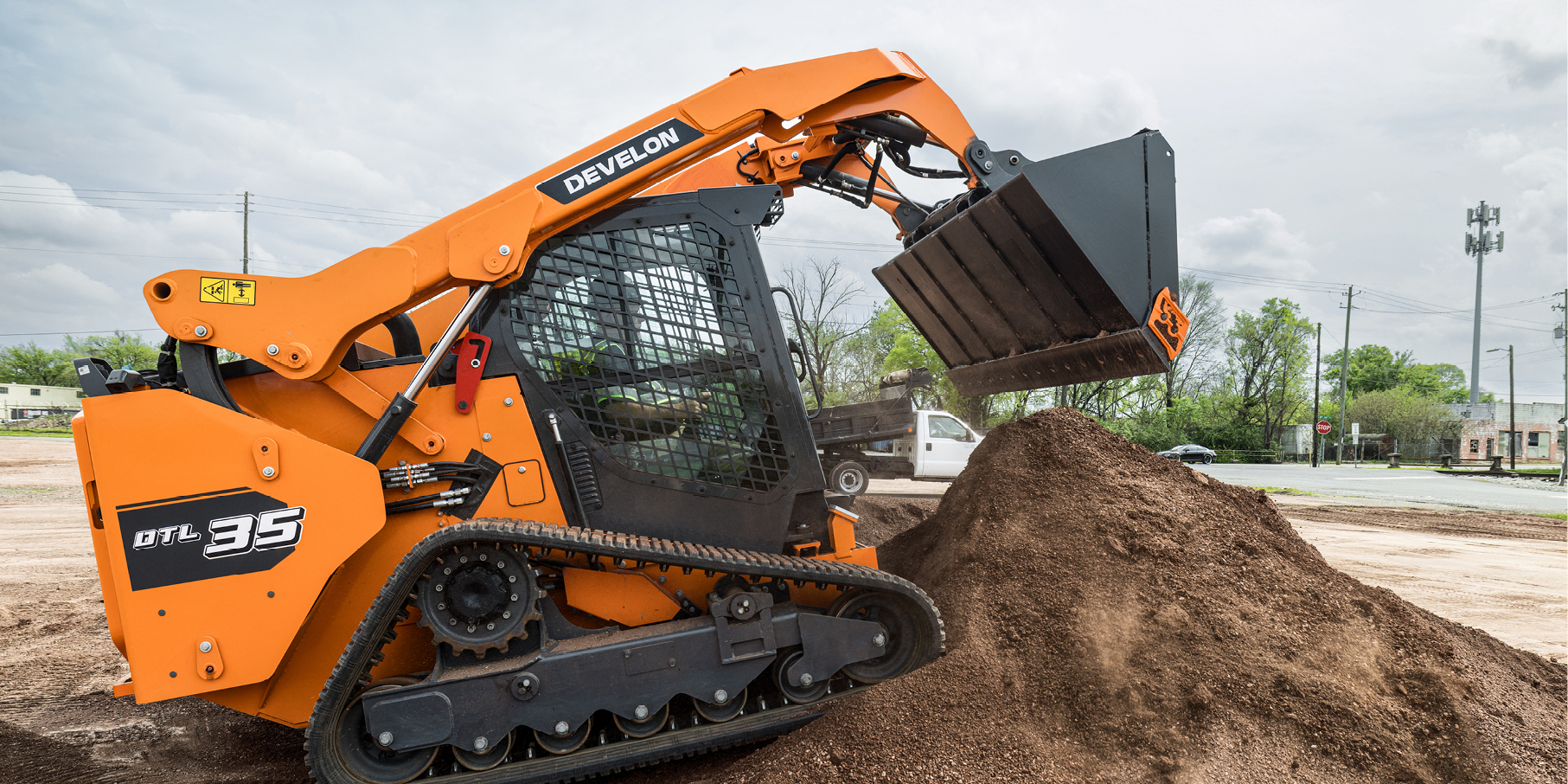 A DEVELON compact track loader dumping a pile of dirt on a job site.