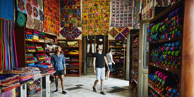 Three friends exploring local market filled with blankets and quilts