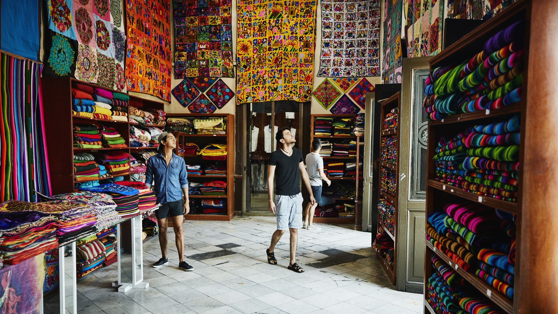 Three friends exploring local market filled with blankets and quilts
