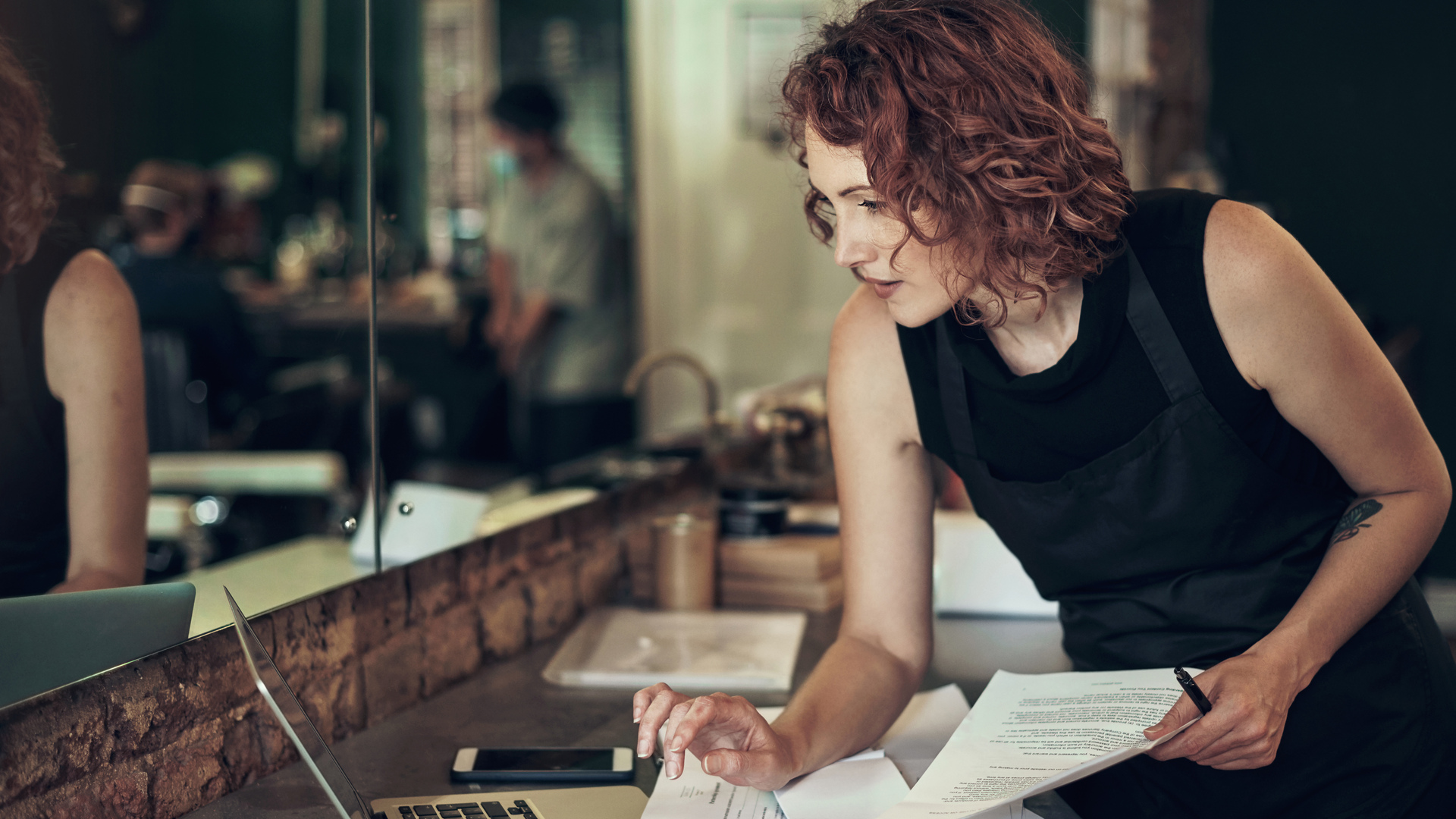 Shot of an attractive young hairdresser standing and using her laptop while calculating her finances in her salon