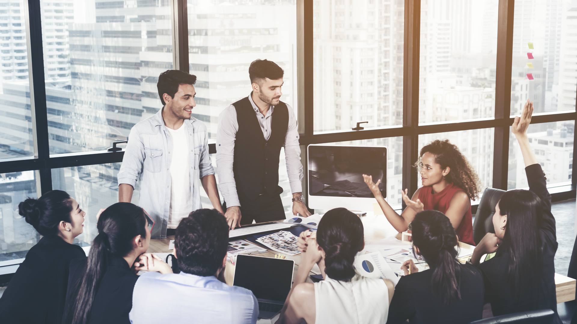 Successful team leader and business owner leading informal in-house business meeting. Business people working on laptops in foreground and glass reflections. Business and entrepreneurship concept