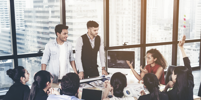 Successful team leader and business owner leading informal in-house business meeting. Business people working on laptops in foreground and glass reflections. Business and entrepreneurship concept