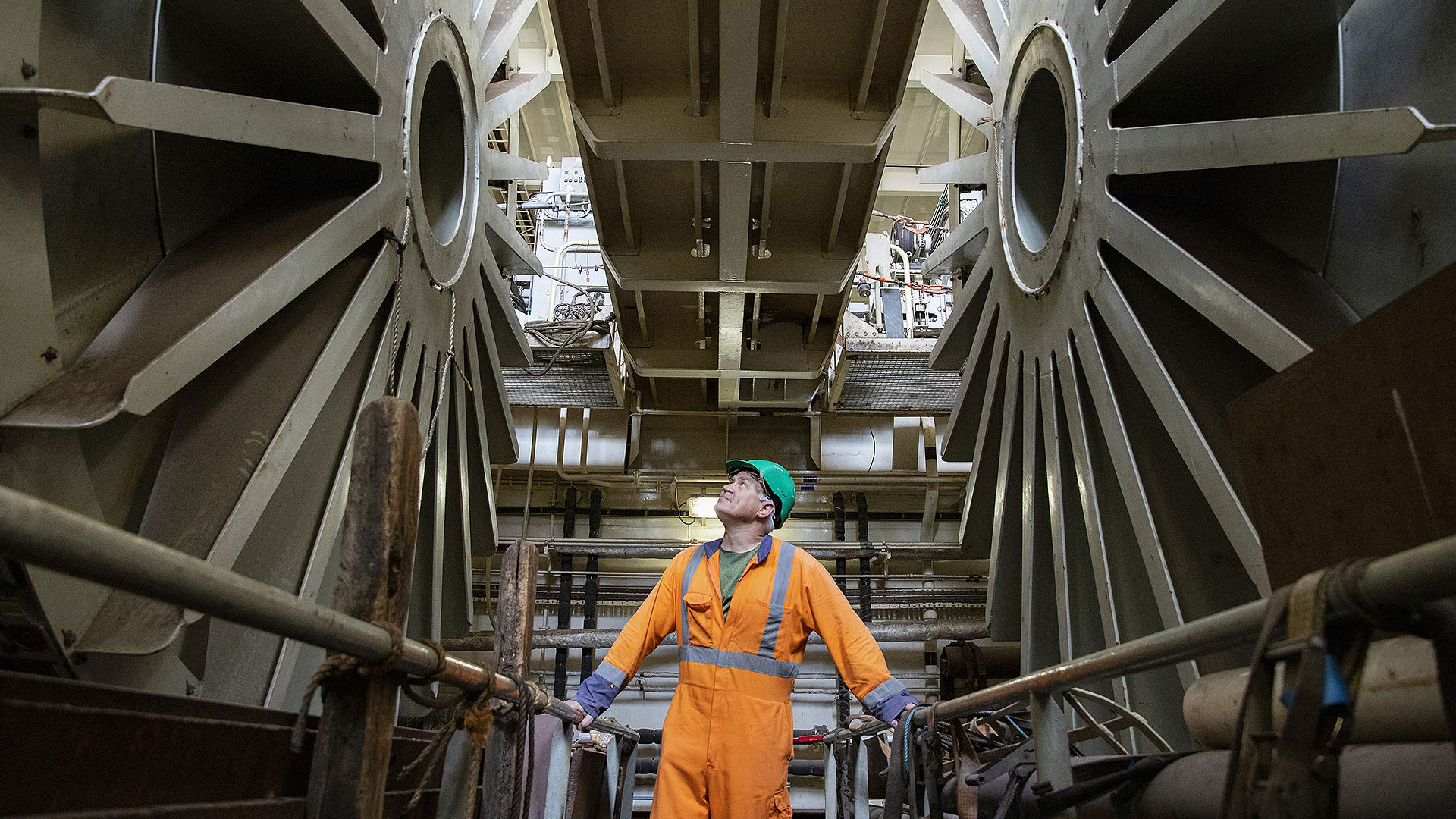 Photo of cable drums that are used to control tension with a worker looking up at them. 