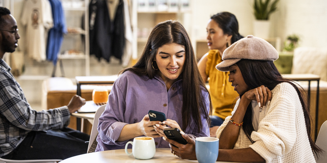 Young women exchanging information with smartphones in modern coffeeshop