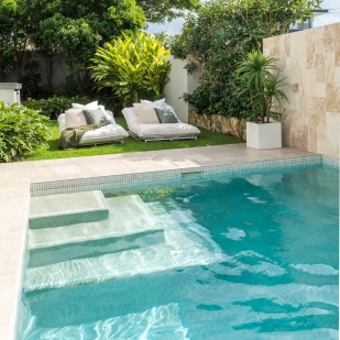 Blue pool on a sunny day with outdoor lounge chairs and a garden
