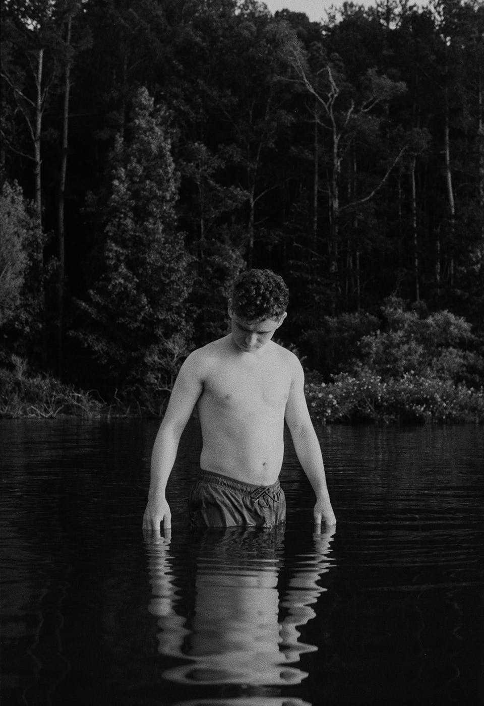 Black and white photograph of a young person standing in a shallow body of water.