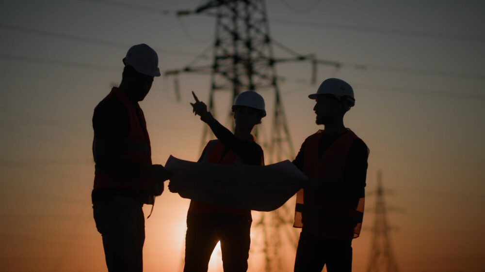 Image of three network workers outside with the sun coming down. There are phone towers in the background