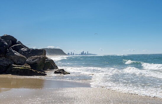 Ocean waves coming up to the rocks at Palm Beach, with the Gold Coast skyline in the background