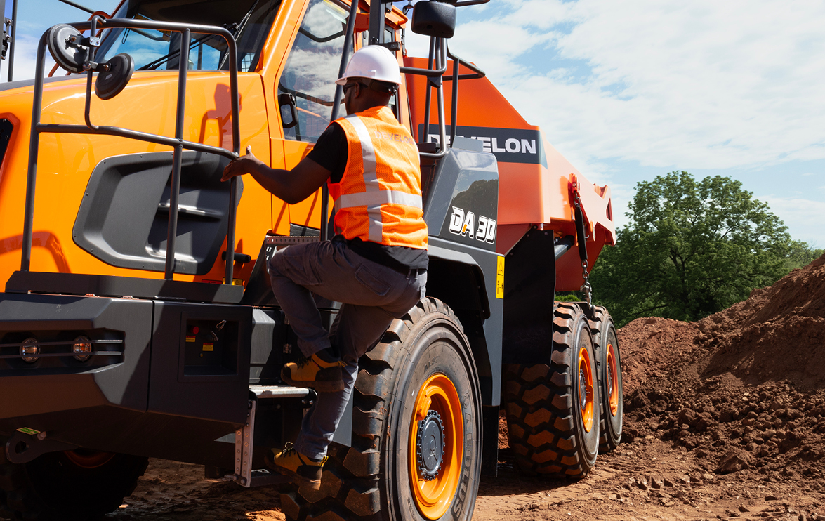 An operator climbs up to the cab of a DEVELON articulated dump truck.