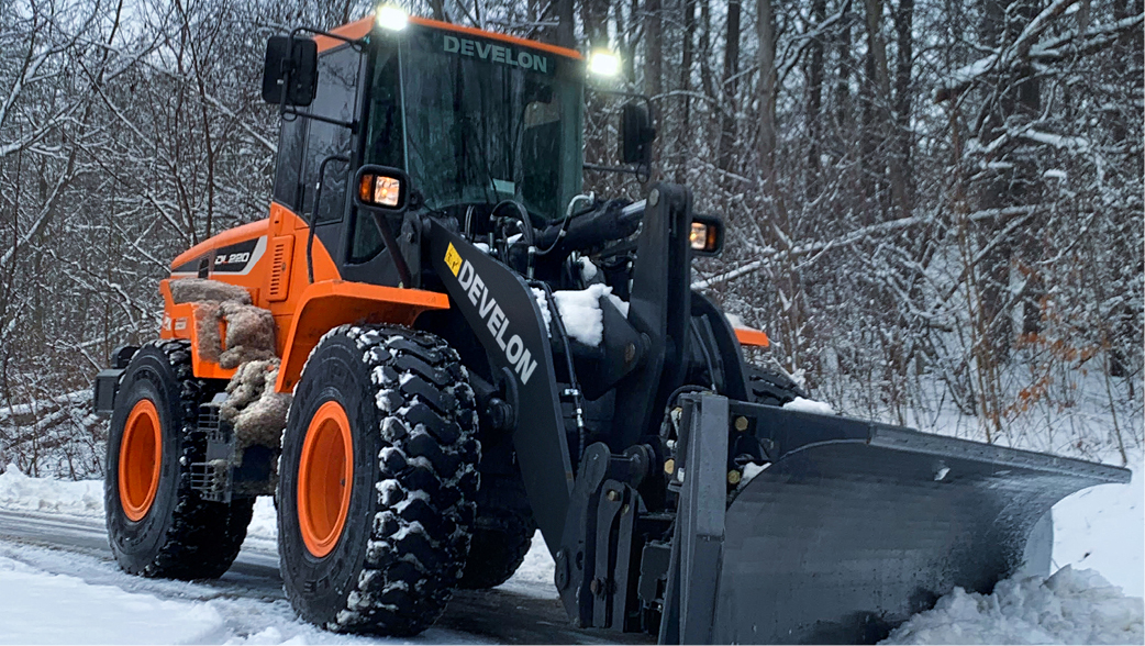 A DEVELON wheel loader clears snow along a road.