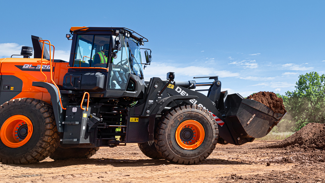 A DEVELON DL320-7 wheel loader travels with a large bucket of dirt on a job site.