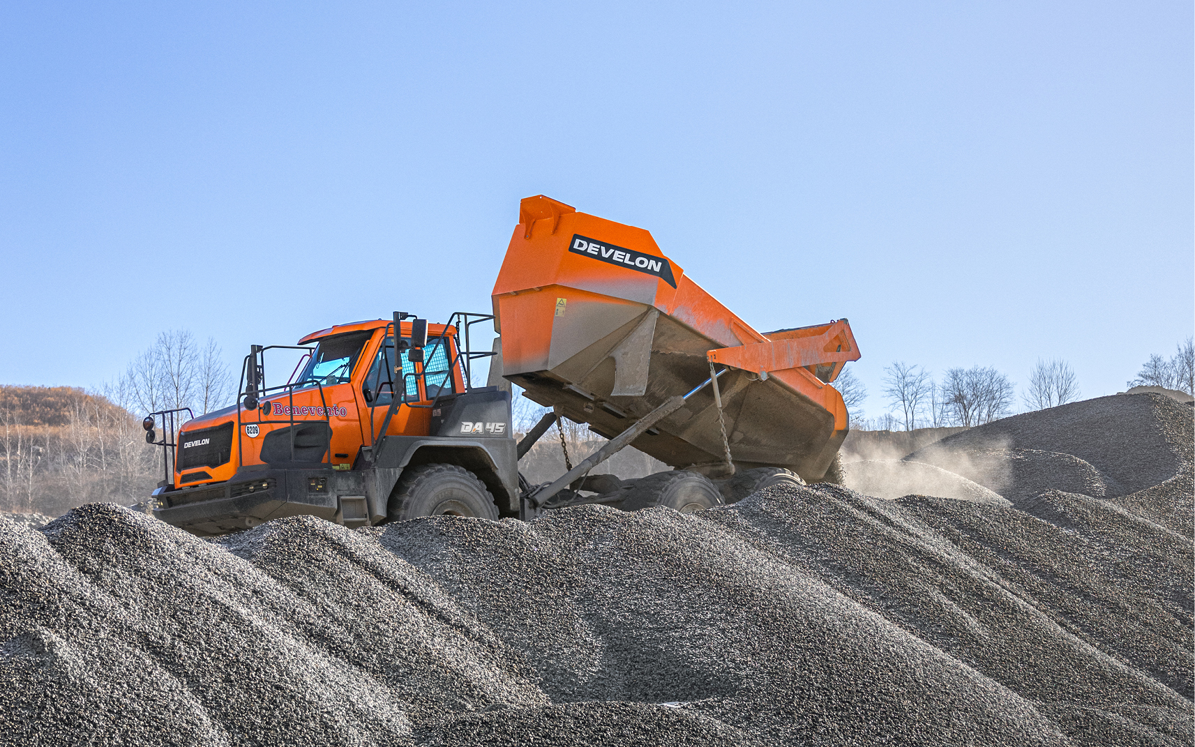 A DEVELON articulated dump truck empties its bed of gravel at a quarry operation.