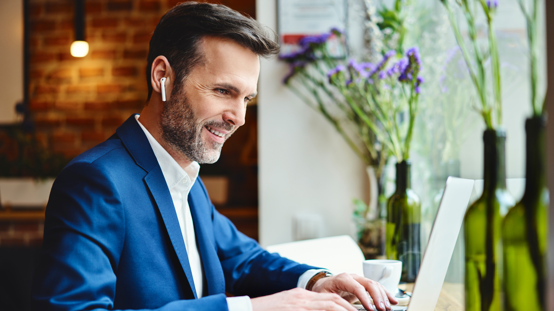 Happy businessman talking through wireless headphones while working on laptop in cafe