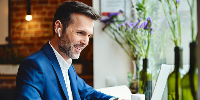 Happy businessman talking through wireless headphones while working on laptop in cafe