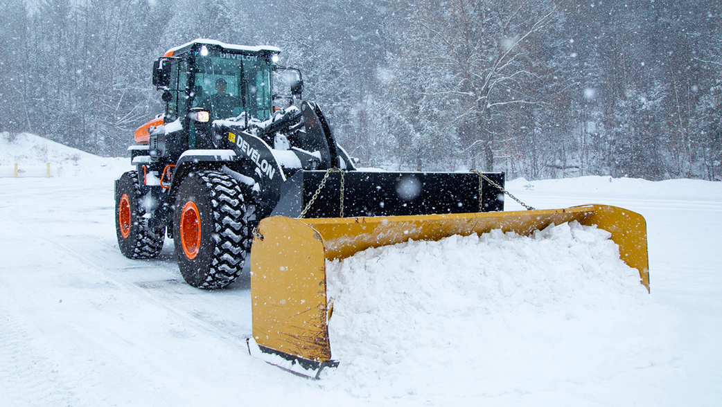 A DEVELON wheel loader clearing snow off a parking lot.