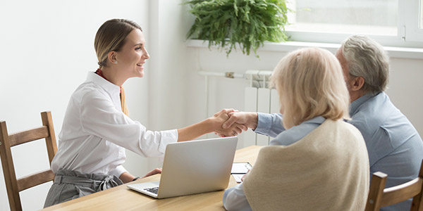 A white woman in a collared shirt shakes hands with an older white man and woman inside of a home