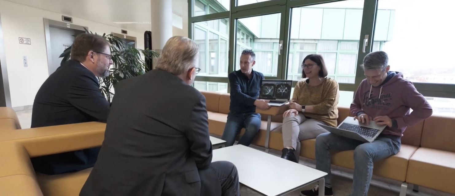 In this image, a group of professionals including GE HealthCare representatives, IT specialists, and project managers from Lower Austrian Regional Hospitals Holding are seen gathered in Waldviertel. They are discussing strategies to enhance healthcare services through improved data management and collaboration, aiming to overcome regional challenges in Austria.