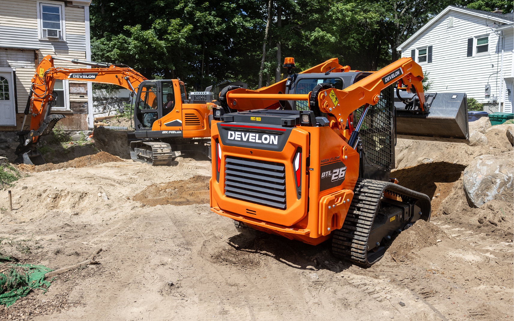 A DEVELON DTL26 CTL with a DEF-free engine working in a tight jobsite near a DEVELON excavator.