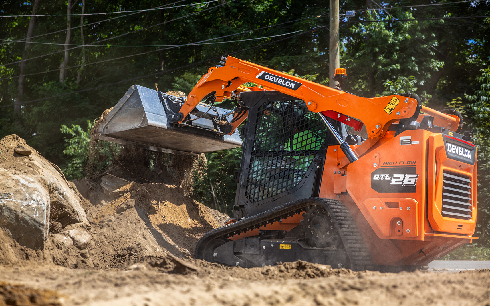 A DEVELON DTL26 CTL with a DEF-free engine unloading dirt into a dirt pile near the road on a jobsite.