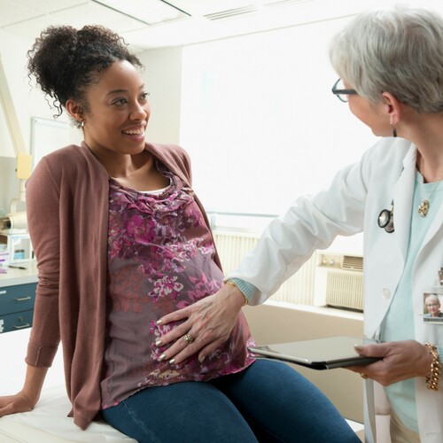 A doctor using a tablet for telehealth meets with a pregnant person in a medical exam room.