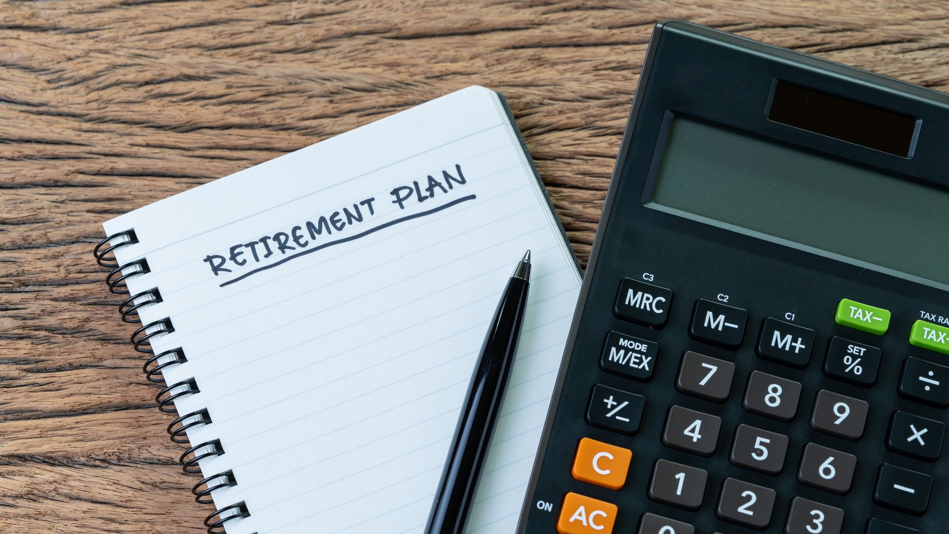 Retirement planning concept, calculator with empty notepad with pen and handwriting underline headline as Retirement Plan on wood table, plan of saving and investment for expense after retire life
