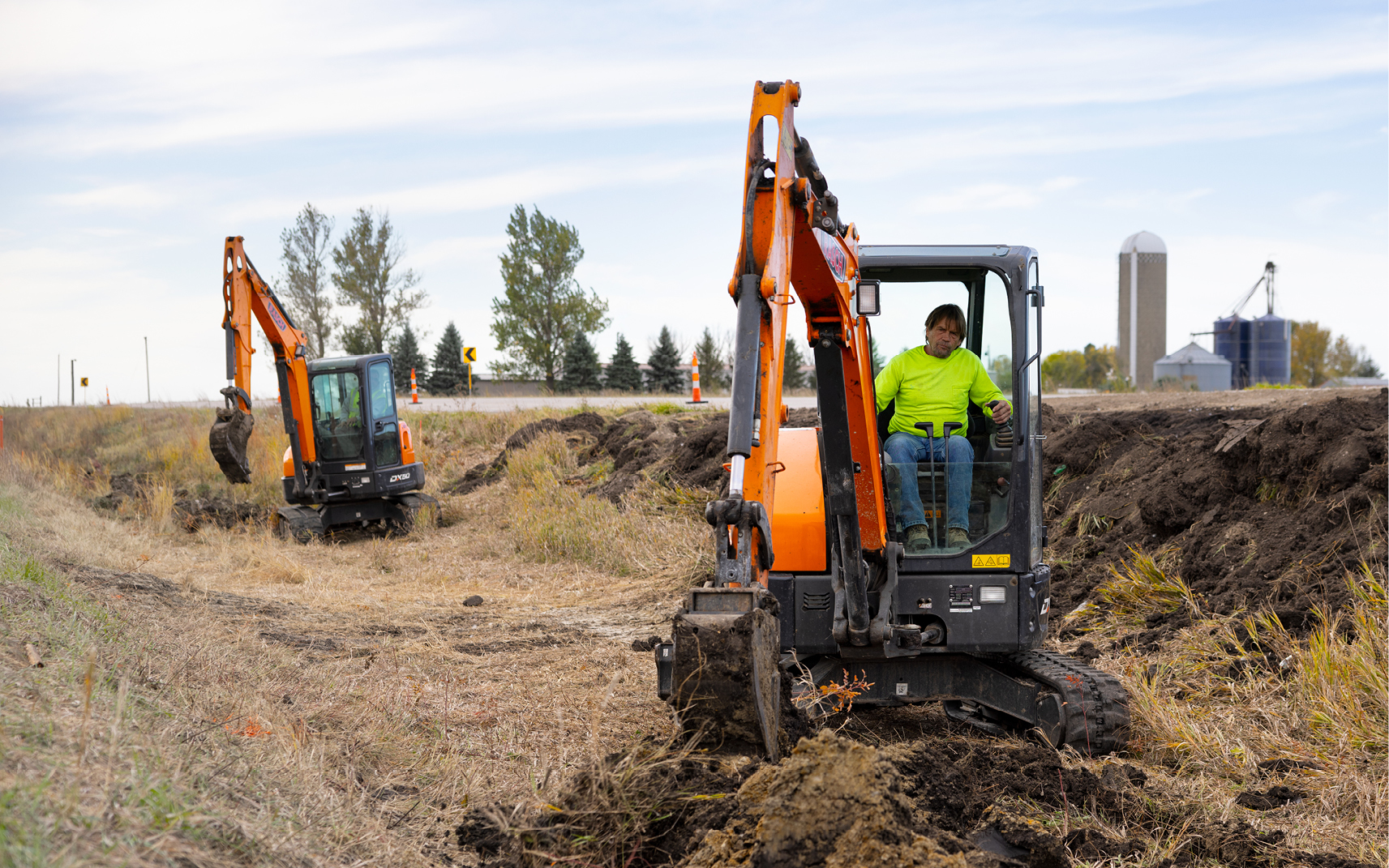 Two mini excavator operators work in tandem on an underground construction project.