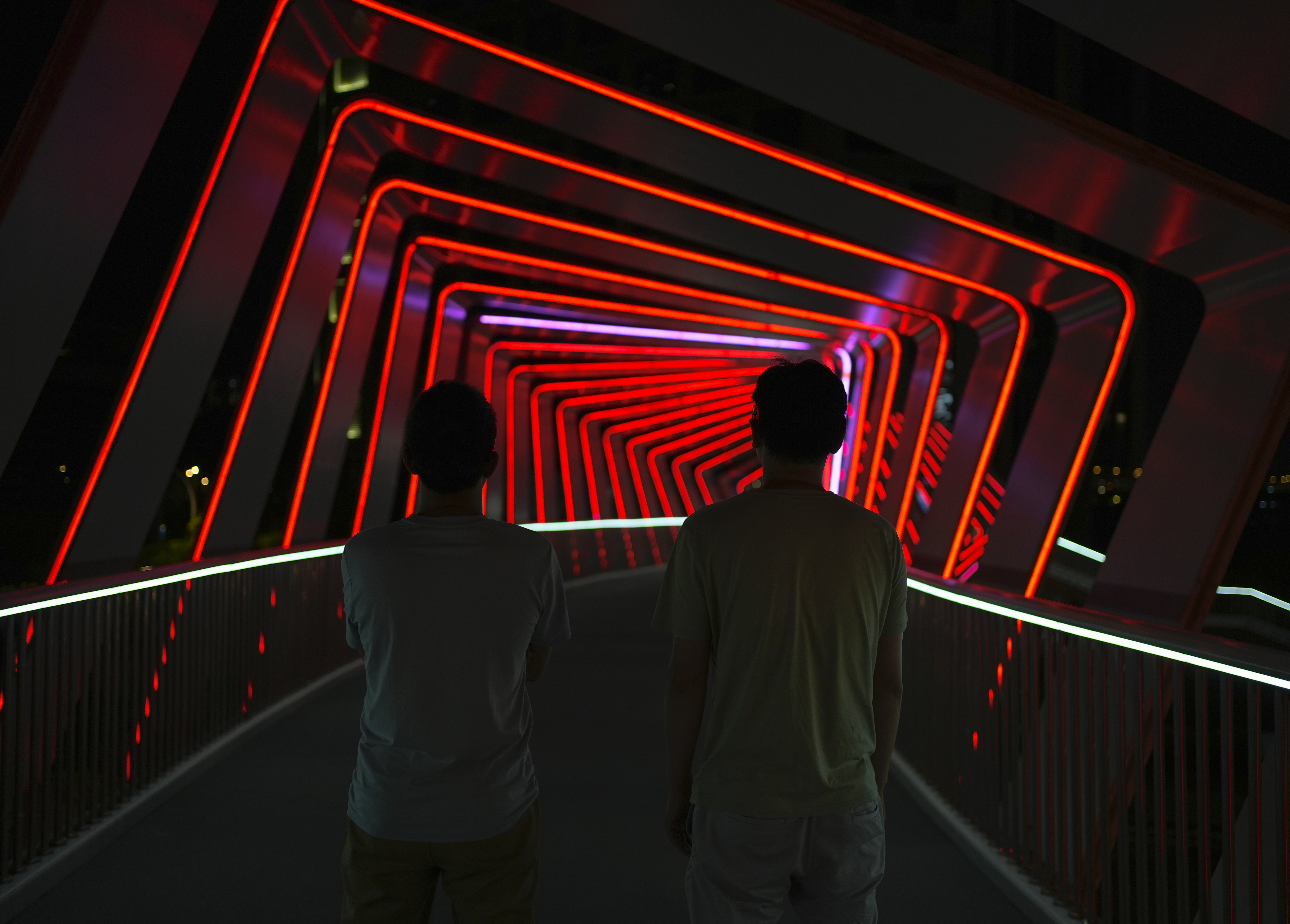 Two people in front of an immersive experience consisting of a walkway down concentric red glowing squares.