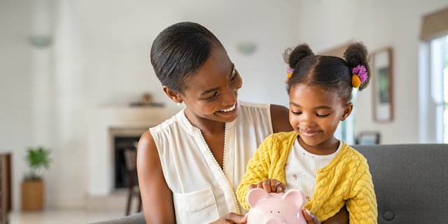 Black woman with daughter holding piggy bank