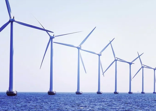 Row of offshore wind turbines aligned over calm blue ocean under a pale sky.