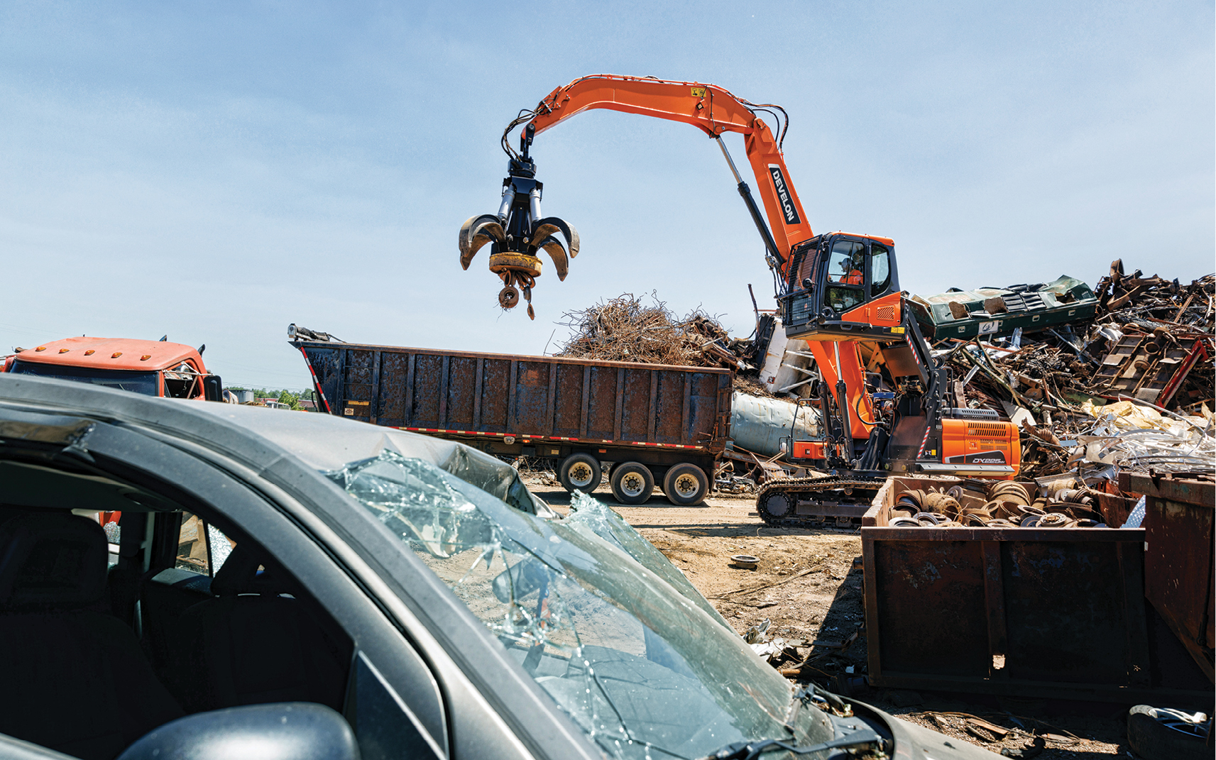 DEVELON DX225MH-5 with an orange-peel grapple attachment lifting scrap metal.