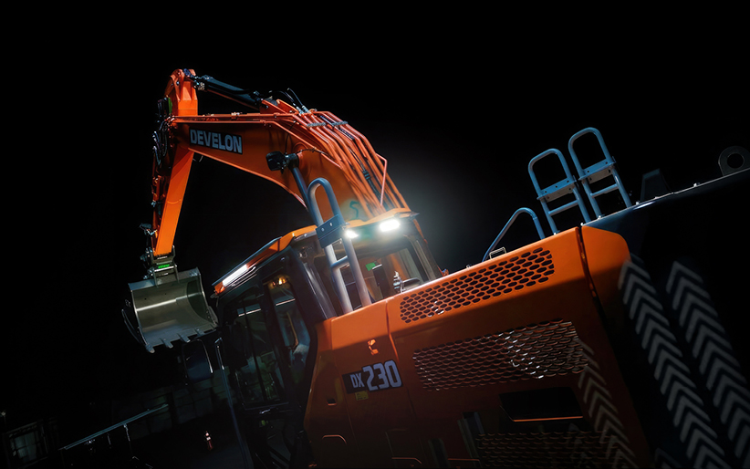 The new DEVELON -9 Series crawler excavator with LED lights on against a black background.