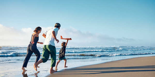 Parents running behind a boy running straight ahead with a model airplane held high in one hand.