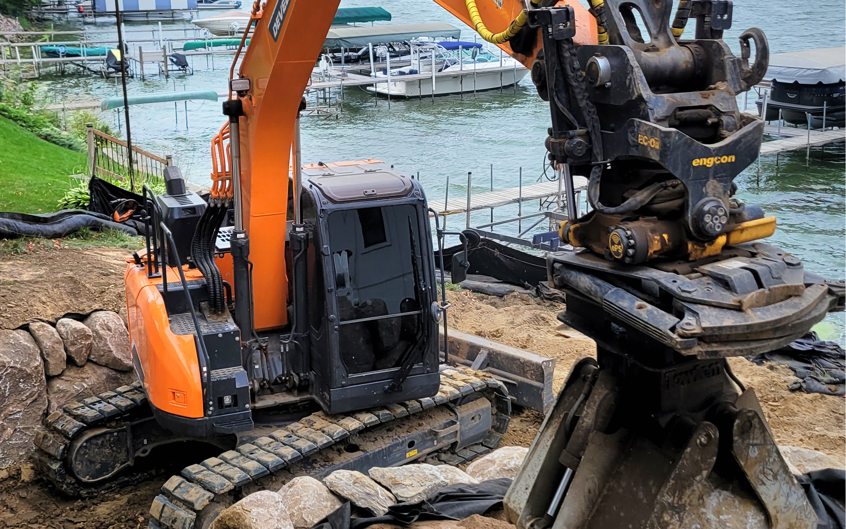 A DEVELON excavator with tiltrotator working on sand.