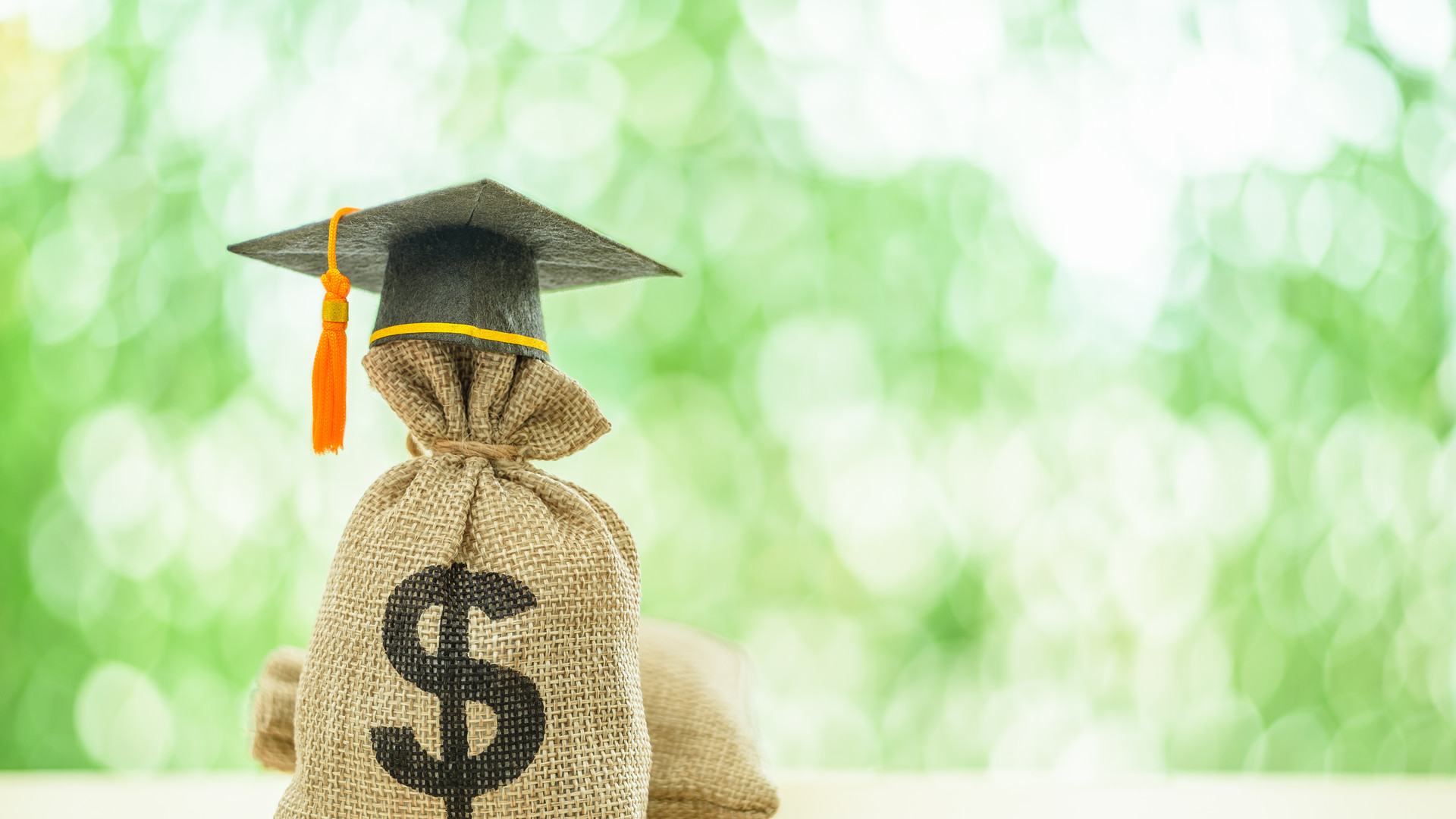 Education or student loan, financial aid and scholarship concept : Mortarboard or graduation cap on top of a US dollar cash bag. Depicting financial assistance for a student's tuition and other costs.