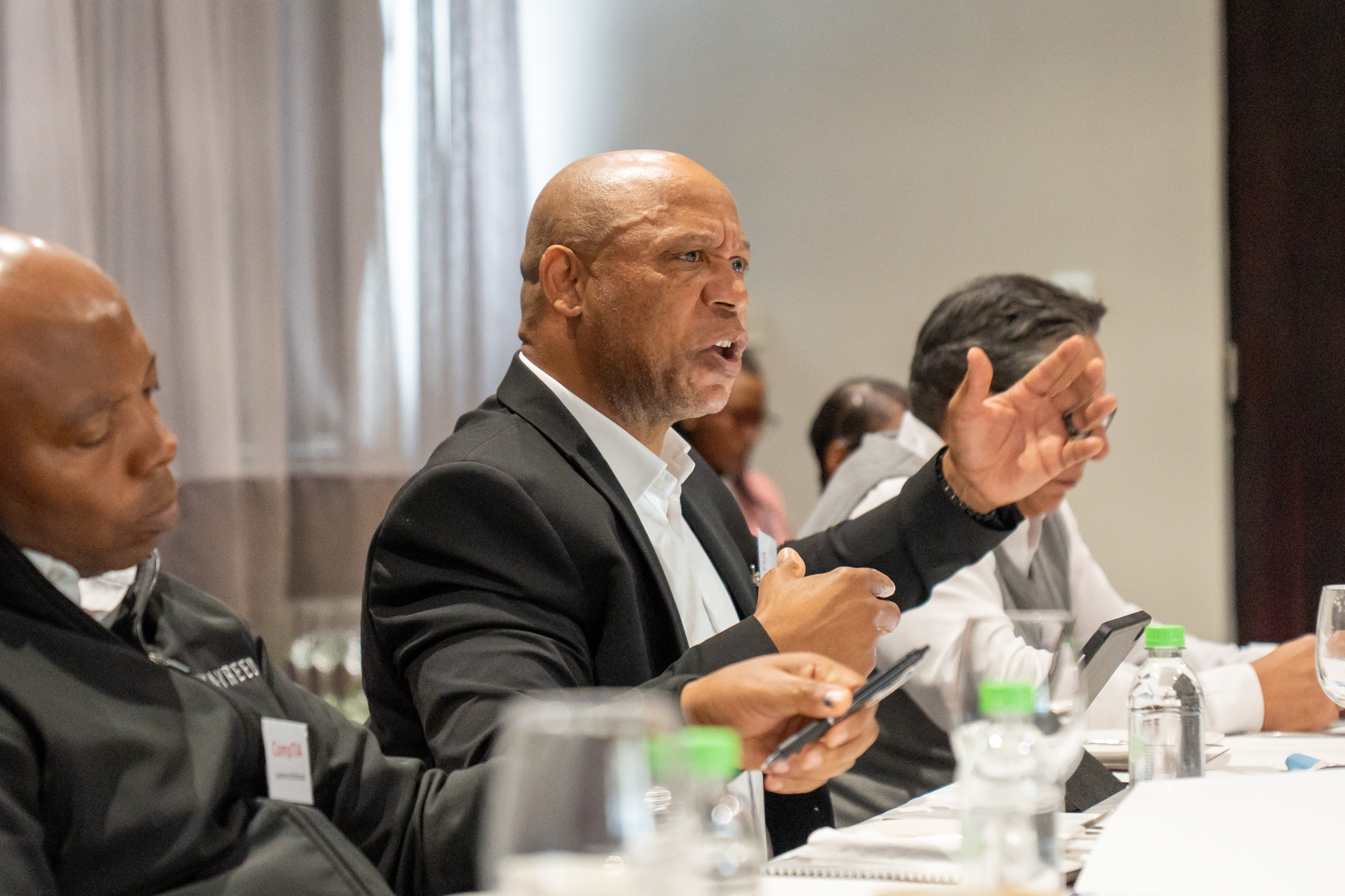 A man speaking animatedly with his hand raised while seated at a conference table with colleagues