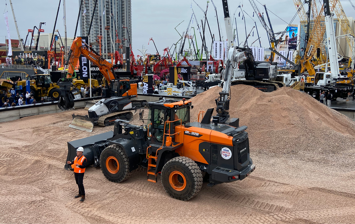 An operator standing in front of a DEVELON DL320 wheel loader during a demonstration at CONEXPO.