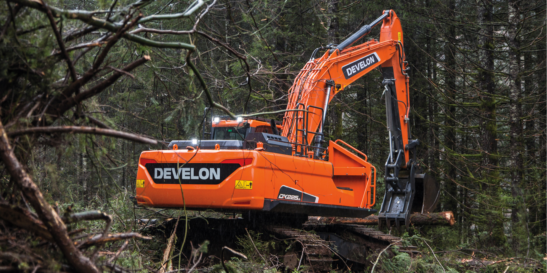 A DEVELON road builder moving trees in a wooded area.