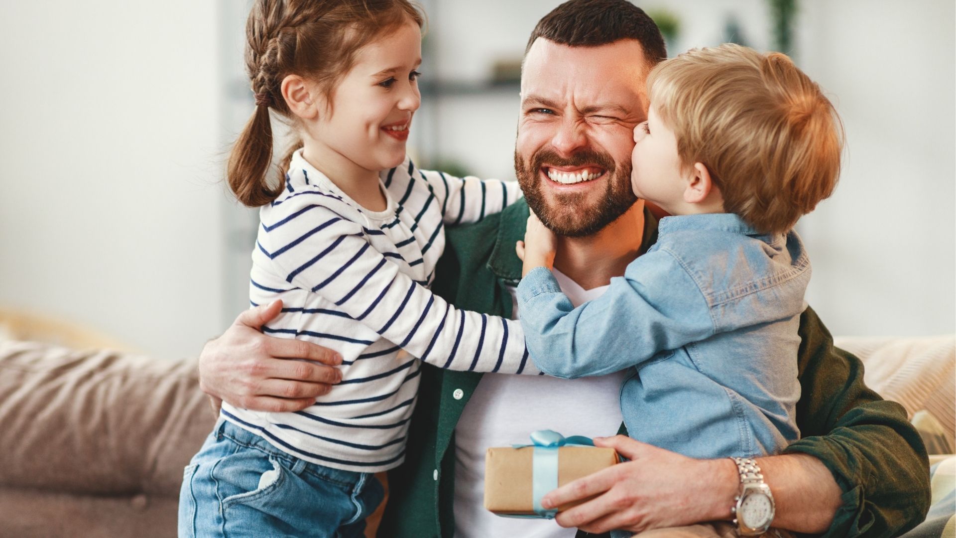 Dad sharing a hug with two children while holding a Father’s Day gift.