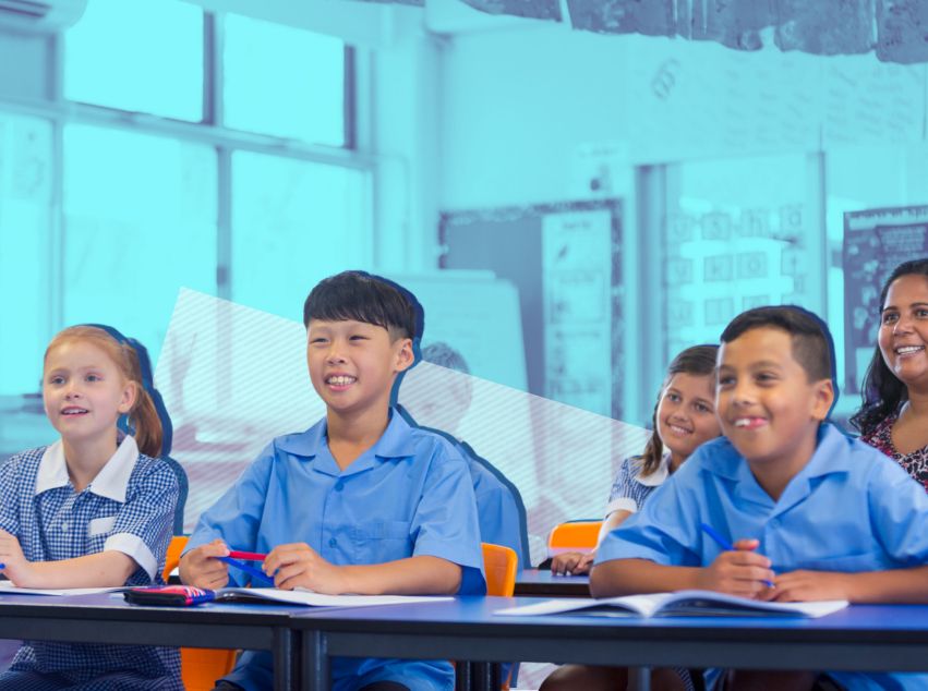 School kids smiling at desks in classroom