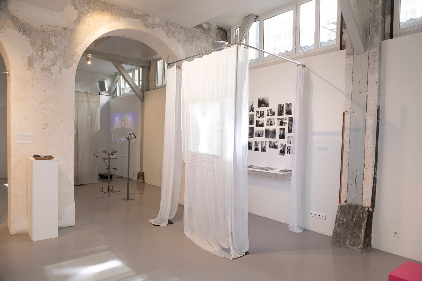 Gallery installation with sheer fabric panels and black-and-white photo wall