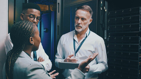 Three IT engineers discussing data center hardware and network architecture beside an open server rack