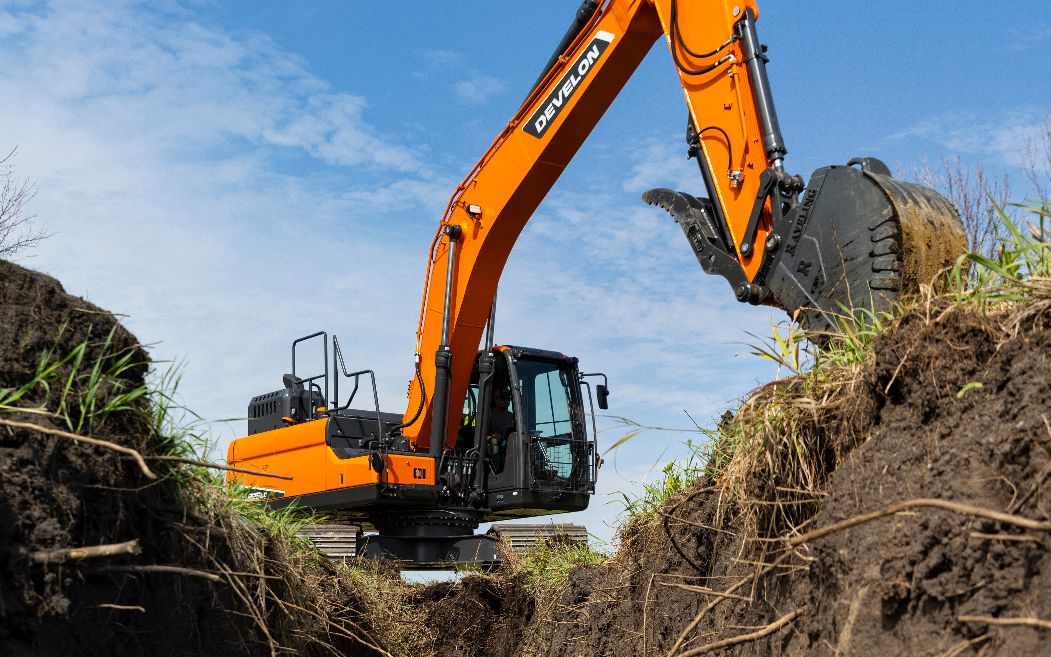 A DEVELON crawler excavator digs a trench with a bucket.